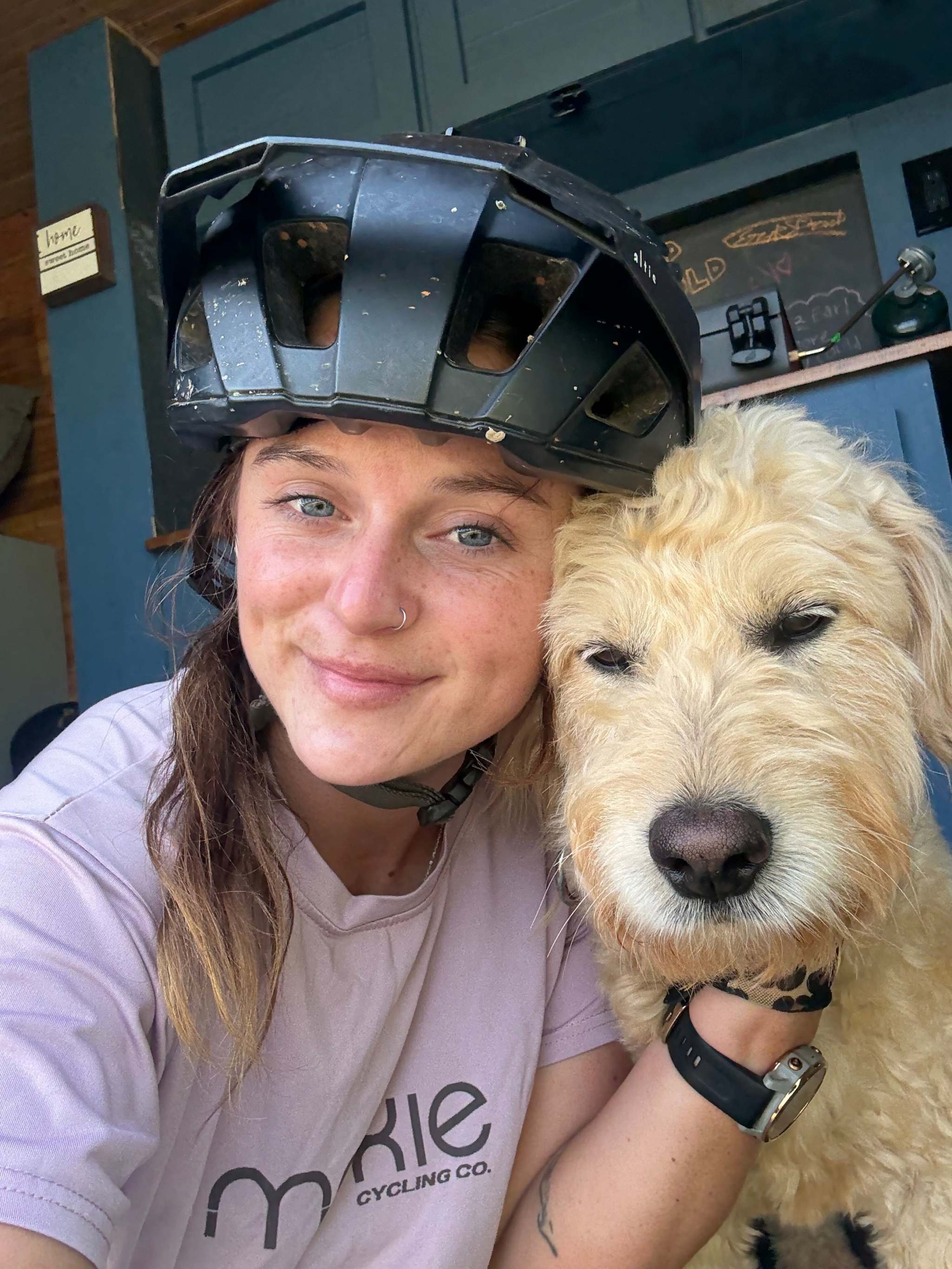 Woman wearing a bike helmet and Trail Dog Collab mountain bike jersey posing with a light-colored dog